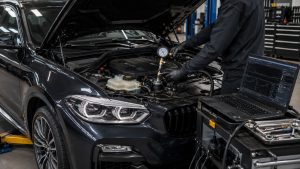 Technician performing BMW cooling system diagnostics with pressure testing equipment and factory-level diagnostic software to identify cooling system leaks and water pump concerns.