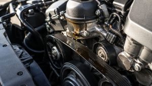 BMW engine with an oil filter housing leak dripping oil onto the serpentine belt, illustrating how oil contamination can damage belt performance and lead to engine repair concerns.